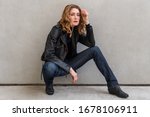 Small photo of A woman poses crouched down in front of a blank wall.