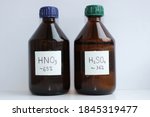 Small photo of Two dark glass bottles of dilute acids, 65 percent nitric acid and about 36 percent sulfuric acid.