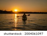 Girl kayaking and taking pause calm sea at midnight in Northern Sweden during light Summer nights. All day around Sun in polar regions.