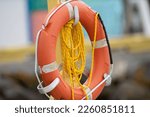 Small photo of A vibrant orange polyethylene life ring hanging on a wooden post with long orange float line. There is reflective table on the preserver with white grab rope. The rescue equipment is a buoyant throw.