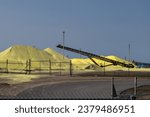Small photo of Mounds of yellow sulfur powder behind a metal fence. The pile is used for oil refinement as a waste product of the fossil fuel industry. The stockpile of the chemical sulfate is for bulk storage.