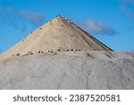 Small photo of A stockpile of salt or sodium chloride road salt, halite, rocksalt stockpiled for winter snow and ice deicing controls. The road salt is piled in one mound with the top portion against a blue sky.