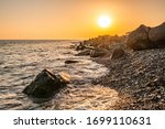 Orange sunset on the seashore with large stones. Large stones with beautiful texture on the background of dawn on the sea. Evening landscape rocky shore