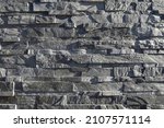 Stone cladding wall made of irregular stacked bricks of gray and black rocks. Panels for exterior, background and texture.