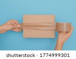 Small photo of human hands wrap up a cardboard box with parcel tape