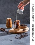 Small photo of Milk Being Poured Into Iced Coffee on a dark table. Ice coffee in a tall glass with cream poured over and coffee beans. Cold coffee drink on a dark background with copy space.