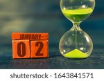 Small photo of january 2nd. Day 2 of month,Handmade wood cube with date month and day and hourglass with green sand. Time passing away. artistic coloring. winter month, day of the year concept