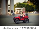 Happy toddler girl driving big red toy sport car, having fun, riding away. Resting on holidays in park outdoor