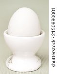 Small photo of White fresh egg in ceramic light eggcup stand on blue background macro retro style