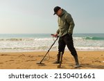Small photo of A man with a metal detector and a shovel on the seashore. A treasure hunter with a metal detector. A man is looking for a treasure. High quality photo