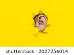 Small photo of Close-up of a left woman's ear through a torn hole in yellow paper. The concept of eavesdropping, espionage, gossip, tabloids and the yellow press. Background with copy space.