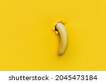 Small photo of A large banana curved downward through a torn hole in yellow paper. Tropical fruit, vegetarianism. Bright background with copy space. The concept of impotence, erectile dysfunction, joke.