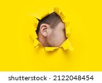 Small photo of A man's ear is visible through a torn hole in the yellow paper. The concept of eavesdropping, espionage, gossip, tabloids and yellow press. Background with copy space.