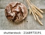 Small photo of Top view of freshly baked rye bread on a yeast-free starter and on a mixture of whole grain, rye and wheat flour. It lies on a napkin, next to a dried flower with grains. Selective focus.