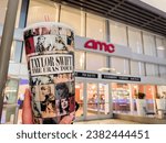 Small photo of San Diego, CA - October 27, 2023: Large Taylor Swift The Eras Tour cup (available from AMC theaters) held up next to AMC exterior logo.