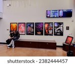 Small photo of San Diego, CA - October 27, 2023: Customers sit next to a row of movie posters at AMC Theater including The Eras Tour Concert Film, the Exorcist, and more.
