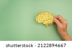 Small photo of Hand holding a brain shape made from paper on a green background. Awareness of Alzheimer's, Parkinson's disease, dementia, stroke, seizure, or mental health. Neurology and Psychology care