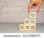 Satisfaction concept. Side view of wooden cubes with stacked smile icons over a table with white brick wall background. Happy mood icons. Feedback emotion scale
