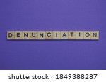 Small photo of gray word denunciation in small square wooden letters with black font on a lilac background