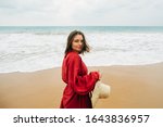 Small photo of Relaxed satisfied young beautiful woman posing on camera by ocean. Get rest or vacation on island. Model in red beach dress look back on camera and pose