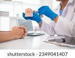 The dentist holds a denture in his hand and shows the patient the position of the problem tooth and the dentist explains how to treat the tooth for the patient to understand. Copy space for text
