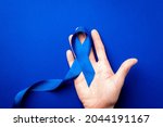 Small photo of Blue ribbon. Awareness prostate cancer of men health in November. Blue ribbon in hands isolated on deep blue background. Symbol of oncology affected man. Copy space