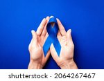 Small photo of Blue ribbon cancer. Awareness prostate cancer of men health in November. Blue ribbon in hands isolated on deep blue background. Symbol of oncology affected man. Copy space
