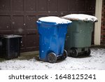 Recycling and Garbage cans in a driveway of a residential home on a snowy day