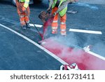 Road workers applying hot red road marking paint on new build road