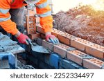 Small photo of Industrial bricklayer laying bricks on cement mix on construction site. Fighting housing crisis by building more affordable houses concept