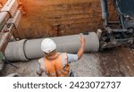 Small photo of Builder installing big diameter concrete drainage pipe protected by trench support system during deep drainage works