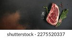 Small photo of New York steak with salt and rosemary, raw marbled beef strip loin steak on a dark background, Long banner format. top view