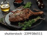 Small photo of Tomahawk rib beef steak with spices and herbs on a dark background. top view. copy space for text.