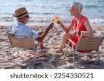 Couple old mature people on the sand at the beach sitting enjoying drink juice and living the moment