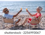 Couple old mature people on the sand at the beach sitting enjoying drink juice and living the moment