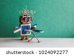 Small photo of Robot helpmate ironing black pants with iron on the board. Green wall gray floor room interior. Creative design toys housework concept Copy space.