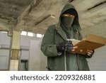 Small photo of Disaster survivor in a post apocalyptic setting, he is wearing a bandana mask and holding paper. Environmental disaster and post-apocalyptic life concept