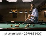 Young caucasian man drinking beer near pool table in bar. Copy space