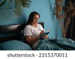 Cute young woman writes a diary while lying in bed in the morning. Rest, sleeping, comfort and people