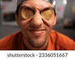 Small photo of Strange stupid man conspiracy theorist in protective foil cap holds two bitcoins in his eyes. Male with bitcoins in eyes. Bitcoin is a cryptocurrency. Fake news concept. Close-up