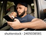Small photo of Male bearded driver with a smartphone in hand and paper cup of hot coffee. Concept of inattention at the wheel, rest and coffee break. Copy space