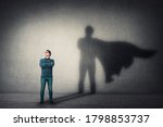 Brave man keeps arms crossed, looks confident, casting a superhero with cape shadow on the wall. Ambition and business success concept. Leadership hero power, motivation and inner strength symbol.