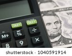 Closed up shot of TAX minus / plus buttons with text TAX RATE on calculator with background of US Dollar banknotes, United States government tax calculation.