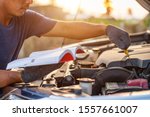 Asian man holding and reading the car user manual or user instruction to checking or fixing engine of modern car. Car maintenance or service before driving concept