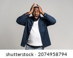 Small photo of Excited astonished African-American guy isolated on grey, shocked multiracial man holding head and staring at camera with opened mouth, dazed dark-skinned male advertising best deal, sale. Copy space