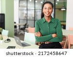 Successful young african-american female entrepreneur, small business owner, female office employee, black businesswoman wearing green casual shirt stands in confident pose with arms crossed