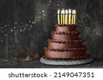 Small photo of Tiered chocolate birthday cake decorated with chocolated frosting and gold birthday candles
