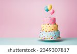 Small photo of Tiered birthday cake with pastel colored tiers decorated with party balloons