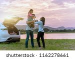 Silhouette the happy family of three people, mother, father and child in front of a sunset sky; asian family are happy sitting in the open trunk of a car; travel nature trip.