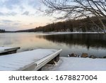 A metal dock sits on a snowy shore while an icy blue sky is reflected in the mirror-like surface of a partially frozen lake in western Maryland, United States.